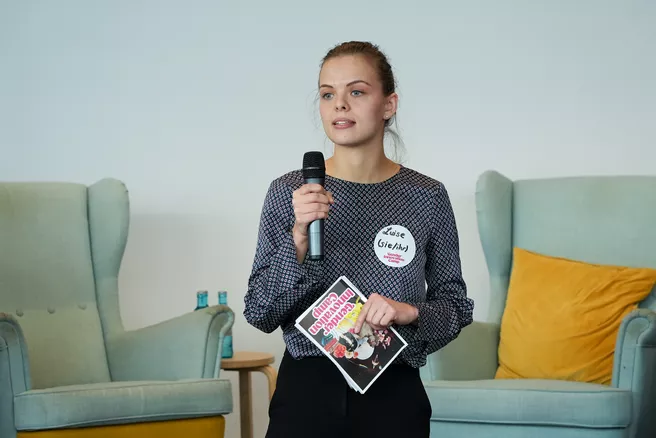 Luise Koch giving a speech in front of two chairs