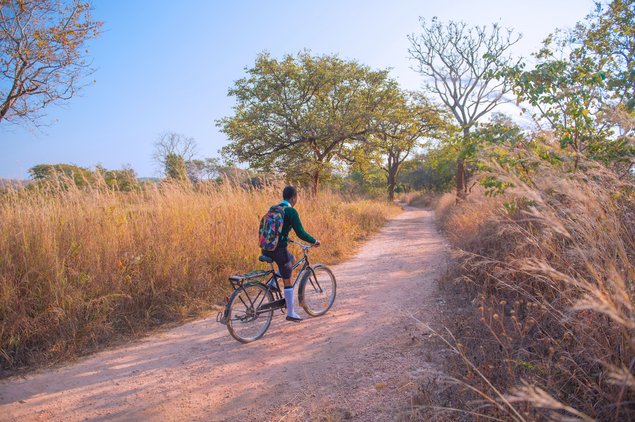 A girl with a school bag rides a WBR-bike on a path through a Zambian plane