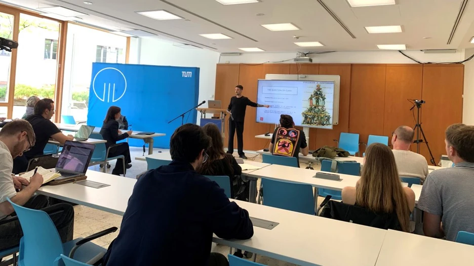 Dr Vincent Harting is standing in front of a screen talking in a lively manner to the participants of his talk in a light flooded room.