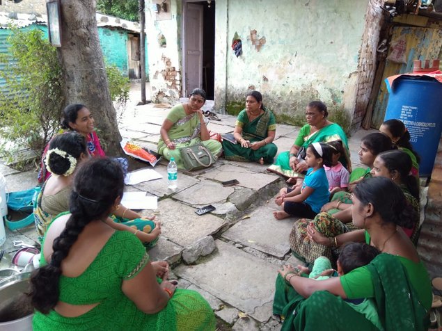 Women and girls sitting in a circle in front of houses